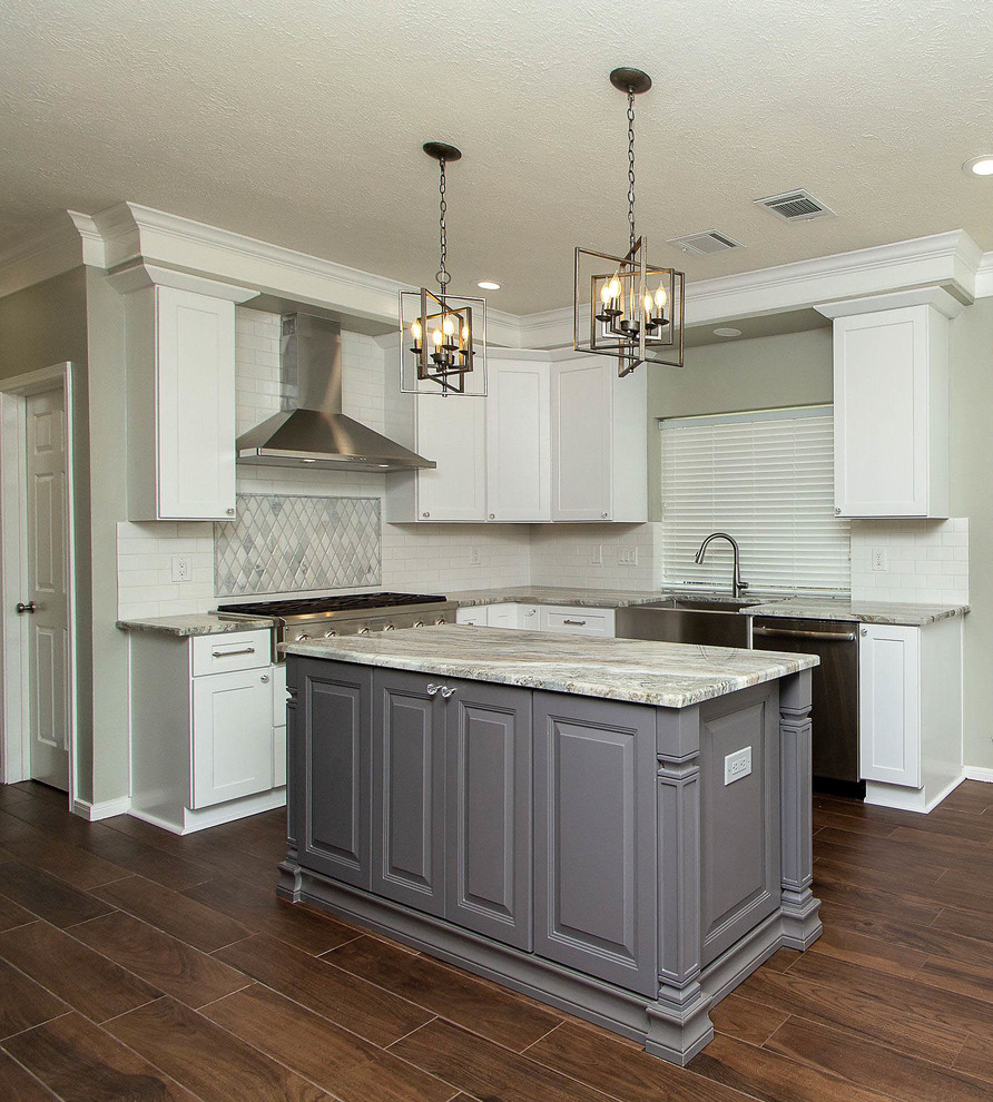 Large traditional u-shaped open plan kitchen in Houston with a farmhouse sink, raised-panel cabinets, white cabinets, granite benchtops, white splashback, subway tile splashback, stainless steel appliances, porcelain floors, with island, brown floor and grey benchtop.
