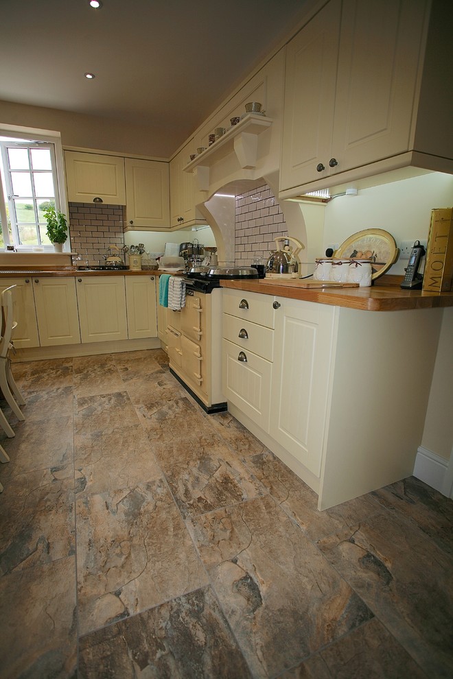 Large country l-shaped eat-in kitchen in Dorset with a double-bowl sink, beaded inset cabinets, beige cabinets, wood benchtops, white splashback, ceramic splashback, ceramic floors, with island and brown floor.