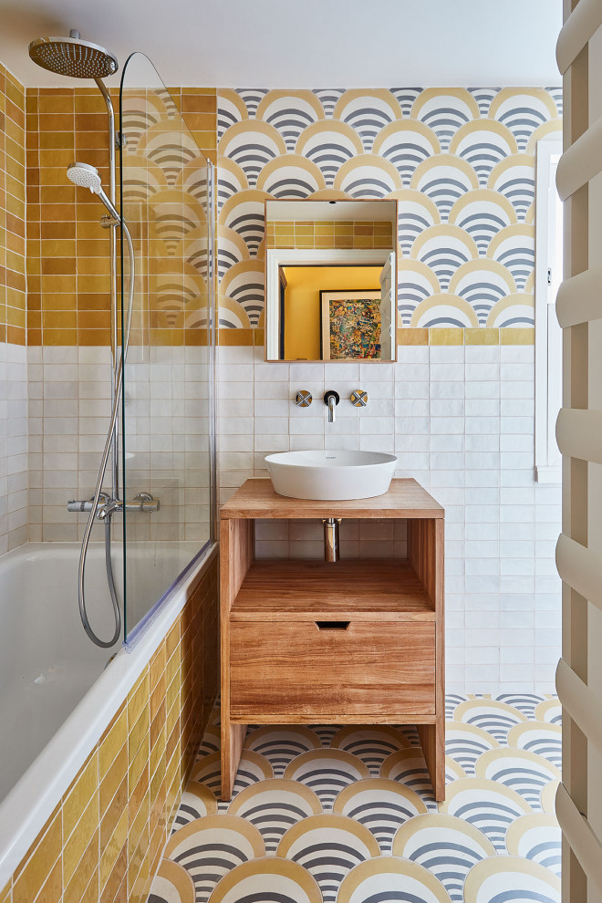 Design ideas for a mid-sized eclectic kids bathroom in London with flat-panel cabinets, light wood cabinets, a drop-in tub, a shower/bathtub combo, a wall-mount toilet, yellow tile, ceramic tile, yellow walls, cement tiles, a trough sink, wood benchtops, yellow floor, a single vanity and a freestanding vanity.