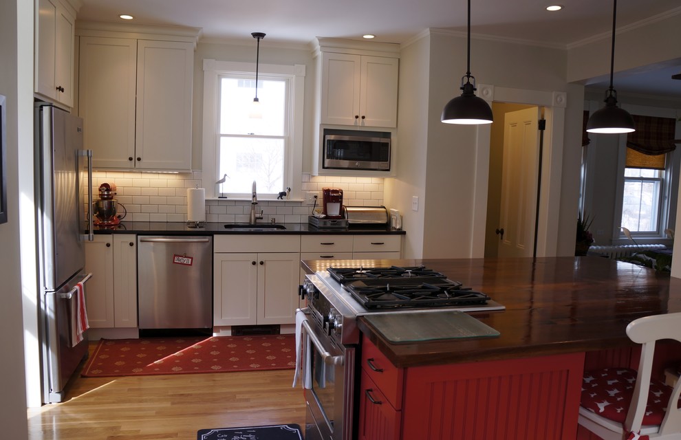 Enclosed kitchen - small rustic l-shaped light wood floor and beige floor enclosed kitchen idea in Boston with an undermount sink, recessed-panel cabinets, granite countertops, white backsplash, subway tile backsplash, stainless steel appliances, an island, white cabinets and black countertops
