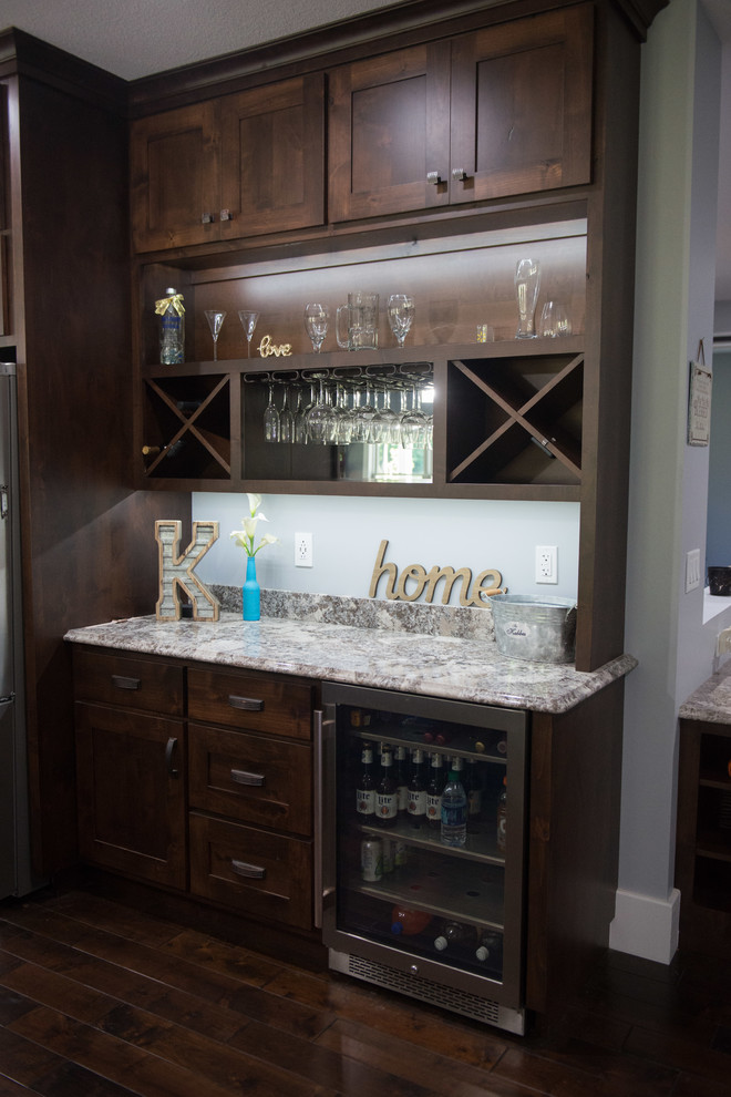 Example of a transitional l-shaped home bar design with an undermount sink, shaker cabinets, dark wood cabinets, granite countertops, stainless steel appliances, an island and multicolored countertops