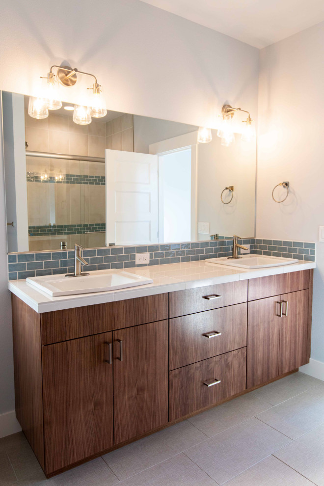 Photo of a mid-sized modern master bathroom in Other with flat-panel cabinets, medium wood cabinets, a two-piece toilet, blue tile, ceramic tile, grey walls, ceramic floors, a drop-in sink, tile benchtops, beige floor, white benchtops, a double vanity, a built-in vanity, an alcove shower and a sliding shower screen.