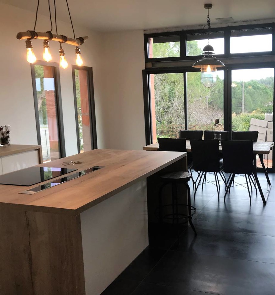 This is an example of a mid-sized industrial galley open plan kitchen in Montpellier with an undermount sink, beaded inset cabinets, beige cabinets, wood benchtops, beige splashback, timber splashback, panelled appliances, ceramic floors, with island, grey floor and brown benchtop.