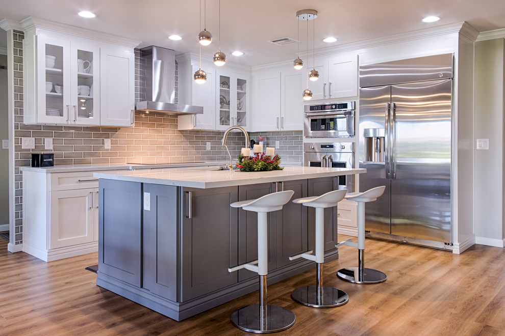 Example of a mid-sized transitional l-shaped laminate floor open concept kitchen design in Phoenix with an undermount sink, shaker cabinets, white cabinets, quartzite countertops, gray backsplash, ceramic backsplash, stainless steel appliances and an island