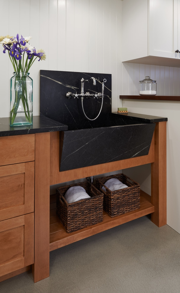 This is an example of a traditional galley utility room in Seattle with a farmhouse sink, shaker cabinets, white cabinets, soapstone benchtops, white walls, concrete floors and a side-by-side washer and dryer.