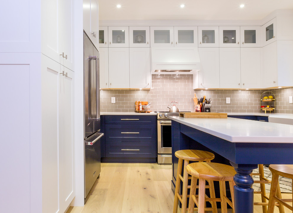 Example of a large transitional u-shaped light wood floor open concept kitchen design with a farmhouse sink, shaker cabinets, blue cabinets, quartz countertops, gray backsplash, glass tile backsplash, stainless steel appliances, an island and white countertops