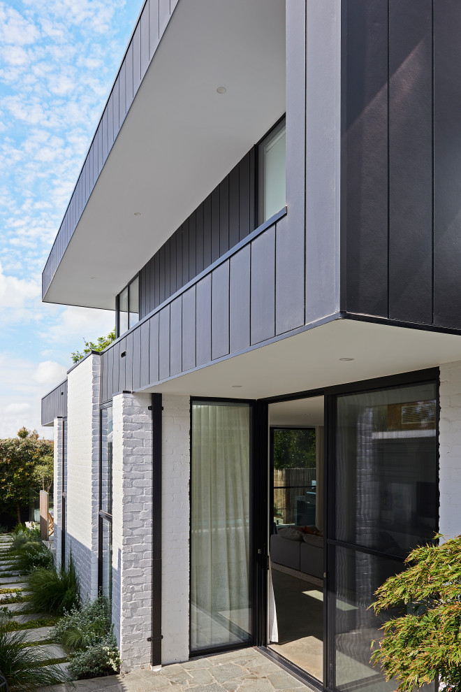 Photo of a mid-sized contemporary two-storey black exterior in Geelong with concrete fiberboard siding, a flat roof and a metal roof.