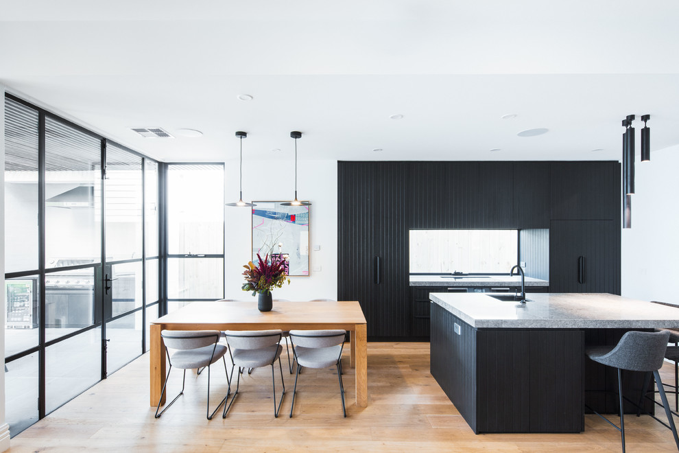 Inspiration for a mid-sized contemporary galley open plan kitchen in Melbourne with black cabinets, quartz benchtops, window splashback, black appliances, with island, grey benchtop, an undermount sink, flat-panel cabinets, medium hardwood floors and brown floor.