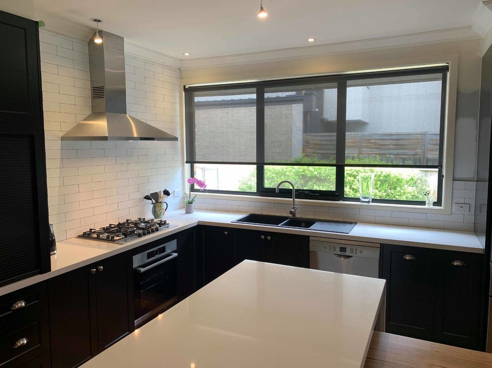 Design ideas for a large contemporary l-shaped open plan kitchen in Melbourne with shaker cabinets, with island, a double-bowl sink, black cabinets, granite benchtops, white splashback, porcelain splashback, stainless steel appliances, medium hardwood floors and white benchtop.