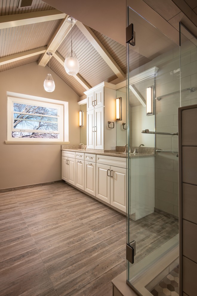 Photo of a mid-sized transitional master bathroom in Omaha with recessed-panel cabinets, white cabinets, a corner shower, a two-piece toilet, white tile, ceramic tile, beige walls, porcelain floors, an undermount sink, engineered quartz benchtops, brown floor, a hinged shower door and beige benchtops.