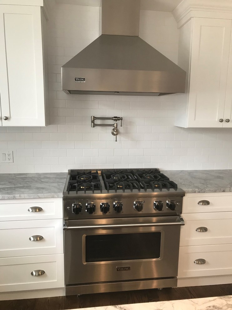 Eat-in kitchen - mid-sized transitional u-shaped dark wood floor and brown floor eat-in kitchen idea in New York with a farmhouse sink, recessed-panel cabinets, white cabinets, wood countertops, white backsplash, limestone backsplash, stainless steel appliances, an island and gray countertops
