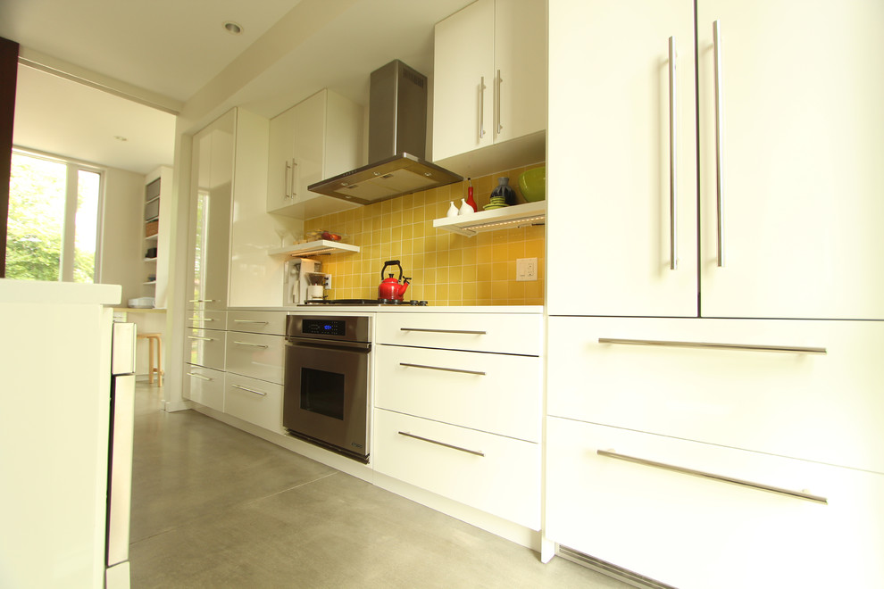 Small modern single-wall open plan kitchen in Other with a double-bowl sink, flat-panel cabinets, white cabinets, quartz benchtops, yellow splashback, ceramic splashback, panelled appliances, concrete floors and with island.