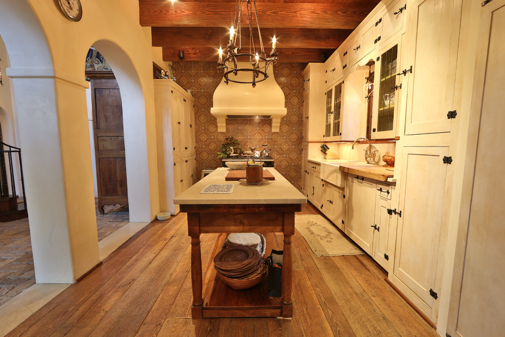 Example of a mid-sized mountain style single-wall medium tone wood floor and brown floor open concept kitchen design in Austin with a farmhouse sink, shaker cabinets, white cabinets, an island, limestone countertops, multicolored backsplash and ceramic backsplash