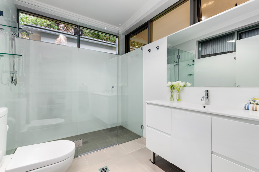 This is an example of a mid-sized contemporary master bathroom in Sydney with an integrated sink, flat-panel cabinets, white cabinets, white walls, a curbless shower, a two-piece toilet, white tile, ceramic tile, ceramic floors, beige floor, a hinged shower door and white benchtops.