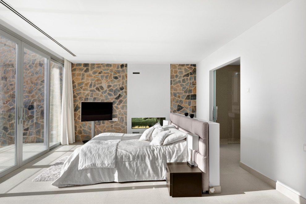 This is an example of a large contemporary master bedroom in Palma de Mallorca with white walls, porcelain floors, a ribbon fireplace, a plaster fireplace surround and beige floor.