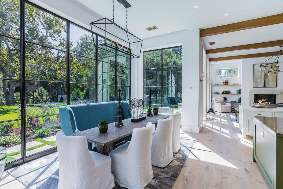 This is an example of an expansive country open plan dining in Los Angeles with white walls, light hardwood floors, a standard fireplace, a stone fireplace surround and beige floor.