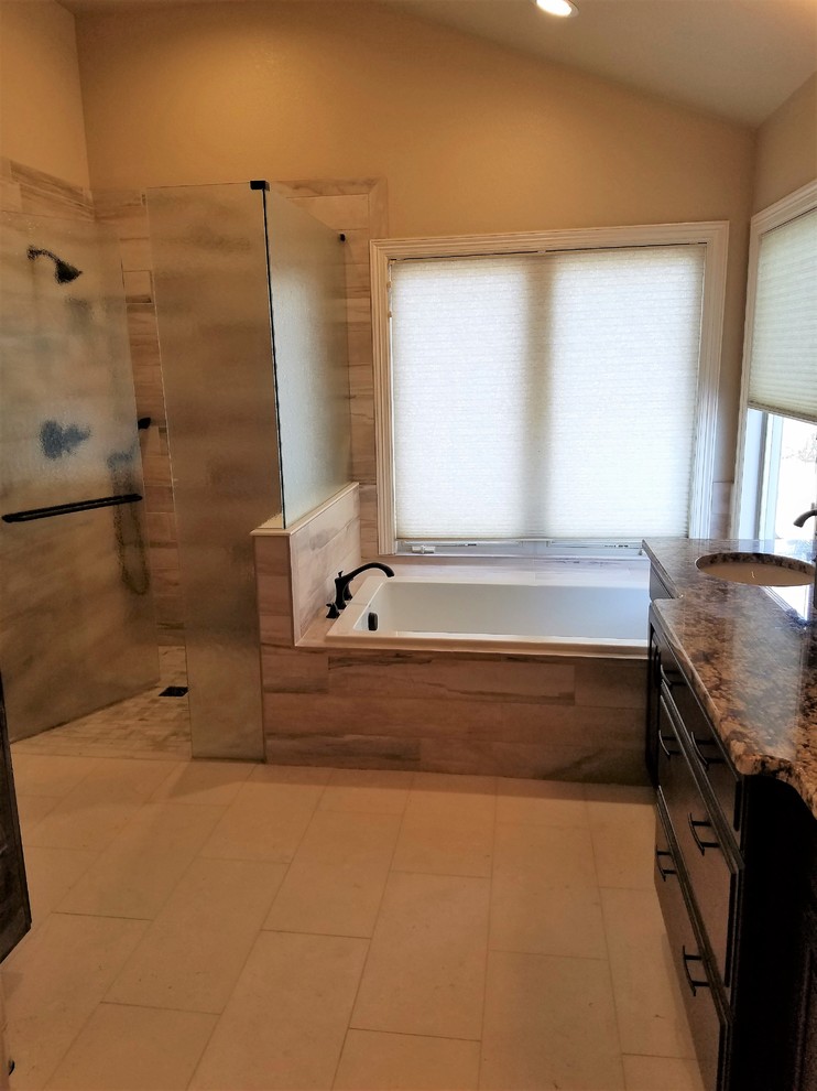 Large eclectic master bathroom in Denver with beaded inset cabinets, dark wood cabinets, a drop-in tub, a curbless shower, beige tile, porcelain tile, beige walls, limestone floors, a drop-in sink, marble benchtops and a hinged shower door.