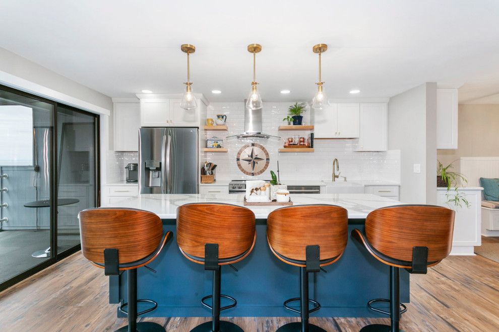 Mid-sized country galley kitchen in Seattle with a farmhouse sink, shaker cabinets, white cabinets, quartz benchtops, white splashback, ceramic splashback, stainless steel appliances, vinyl floors, with island, brown floor and beige benchtop.