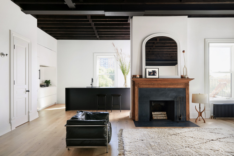 Photo of a modern open concept living room in New York with white walls, light hardwood floors, a standard fireplace, a wood fireplace surround and exposed beam.