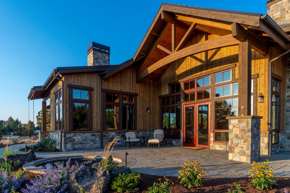 Example of a large mountain style backyard stone patio design with a fireplace and a roof extension