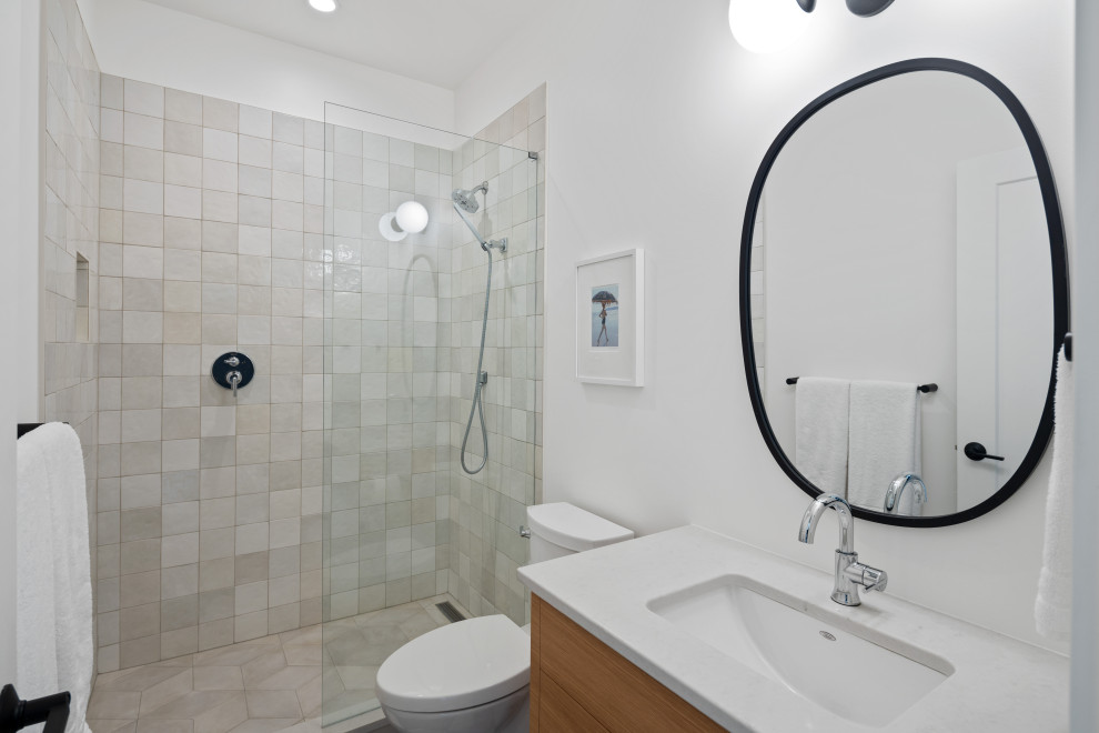 Bild på ett vintage vit vitt badrum med dusch, med släta luckor, bruna skåp, en dusch i en alkov, en toalettstol med separat cisternkåpa, grå kakel, keramikplattor, grå väggar, linoleumgolv, ett undermonterad handfat, bänkskiva i kvarts, vitt golv och med dusch som är öppen