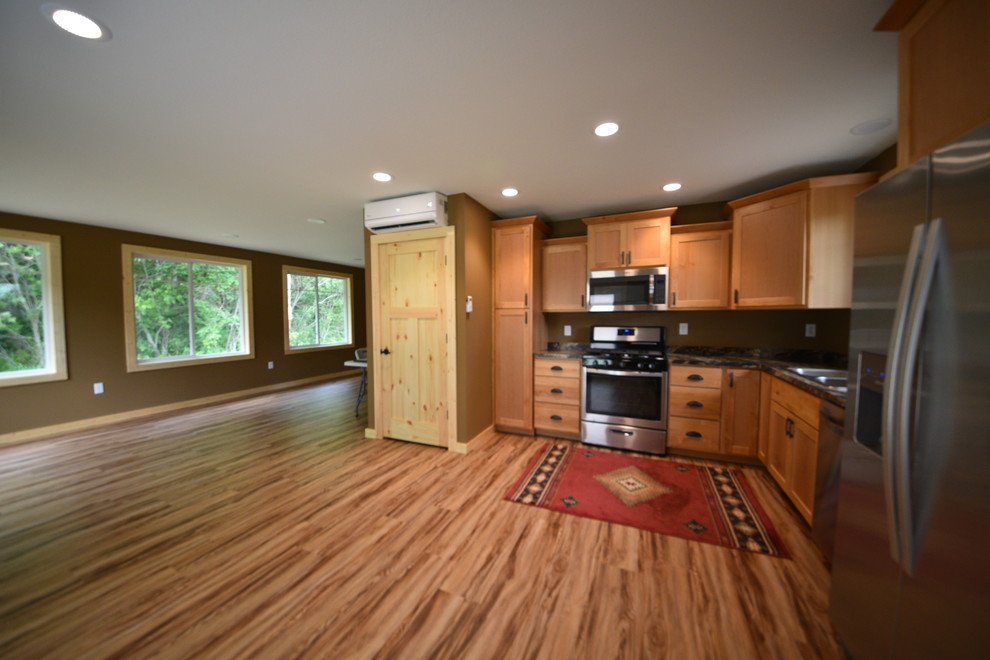 Inspiration for a mid-sized rustic l-shaped laminate floor and brown floor eat-in kitchen remodel in Minneapolis with a drop-in sink, flat-panel cabinets, light wood cabinets, granite countertops, black backsplash, stainless steel appliances and no island