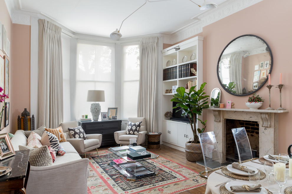 Photo of a transitional open concept living room in London with pink walls, medium hardwood floors, a standard fireplace, a built-in media wall and brown floor.
