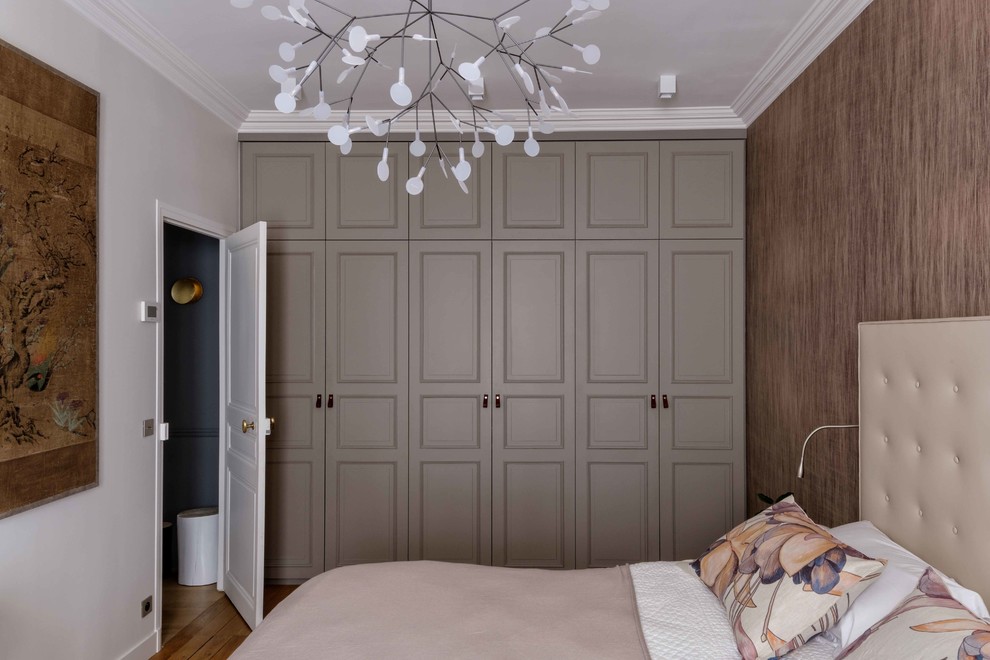 Photo of a large transitional gender-neutral built-in wardrobe in Paris with grey cabinets, light hardwood floors, brown floor and raised-panel cabinets.