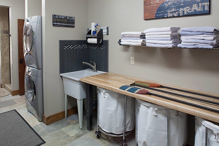 This is an example of a mid-sized country dedicated laundry room in Other with flat-panel cabinets, marble benchtops, white walls, ceramic floors, a stacked washer and dryer and an utility sink.