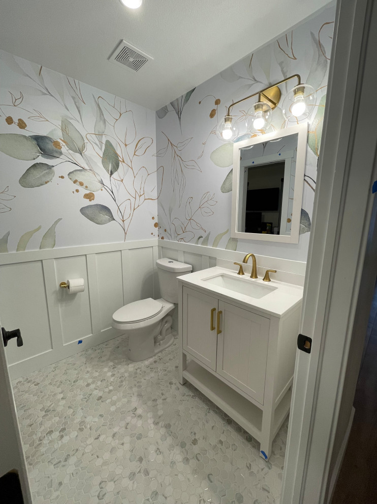 This is an example of a small transitional powder room in Denver with white cabinets, marble floors, white benchtops, a freestanding vanity, furniture-like cabinets, engineered quartz benchtops and wallpaper.