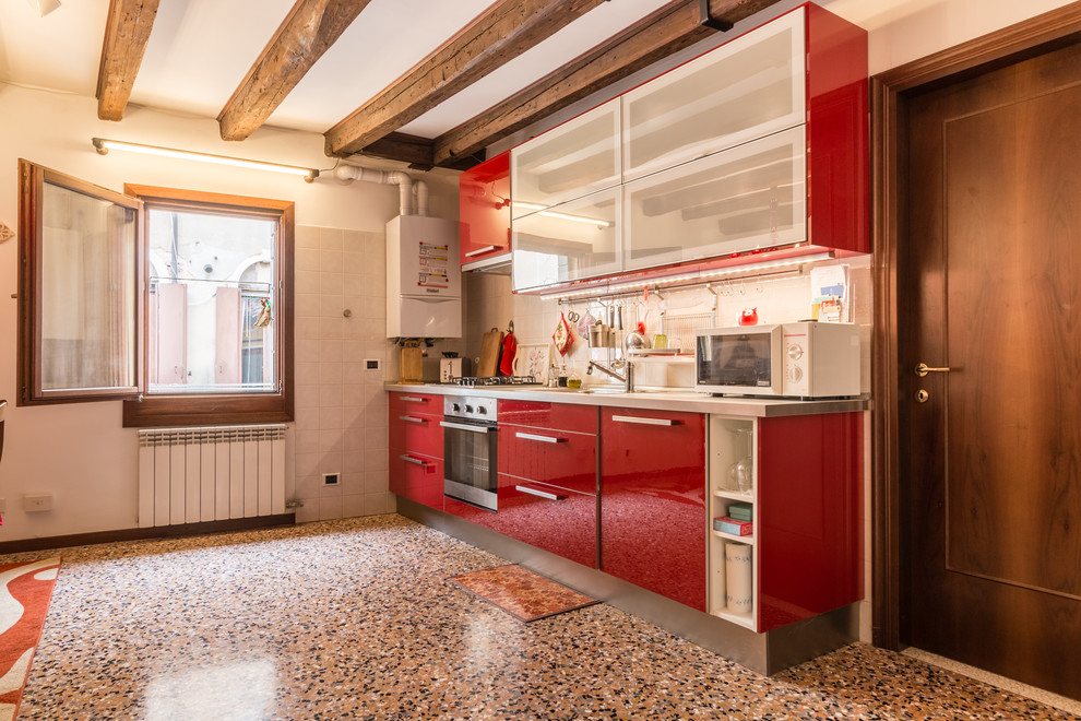 Design ideas for an eclectic single-wall eat-in kitchen in Venice with a drop-in sink, flat-panel cabinets, red cabinets, stainless steel benchtops, grey splashback, black appliances, no island and multi-coloured floor.