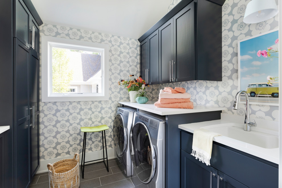 Design ideas for a transitional galley laundry room in Minneapolis with an undermount sink, flat-panel cabinets, blue cabinets, quartz benchtops, beige walls, ceramic floors, a side-by-side washer and dryer, grey floor, wallpaper and white benchtop.