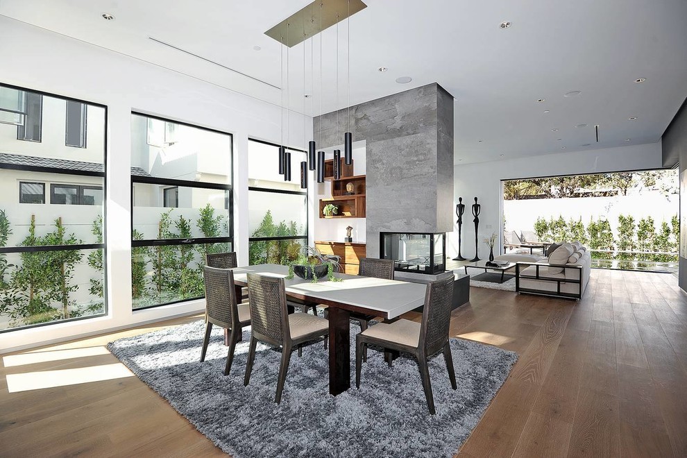 This is an example of a large contemporary open plan dining in Los Angeles with white walls, medium hardwood floors and a two-sided fireplace.
