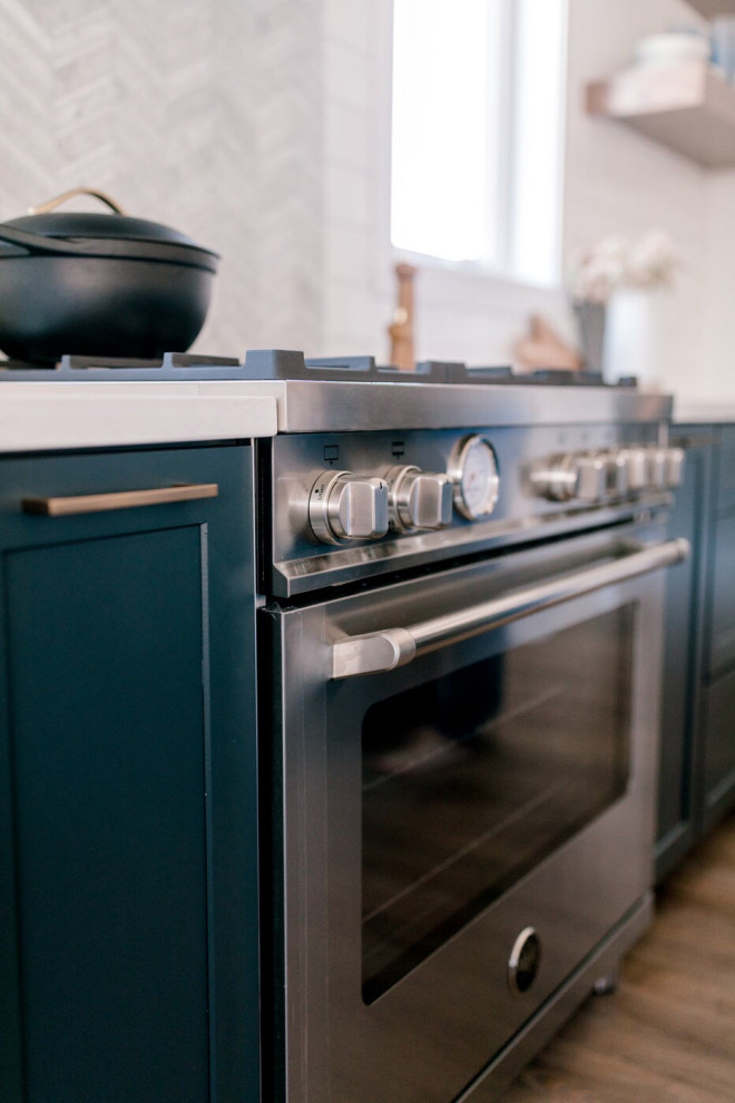 Foto di una cucina stile marinaro con ante verdi, paraspruzzi grigio, elettrodomestici in acciaio inossidabile, pavimento in legno massello medio, pavimento marrone e top bianco