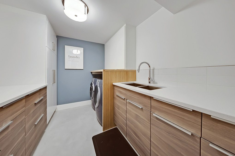 This is an example of a mid-sized contemporary galley dedicated laundry room in Calgary with a double-bowl sink, flat-panel cabinets, medium wood cabinets, white walls, a side-by-side washer and dryer, white floor and white benchtop.