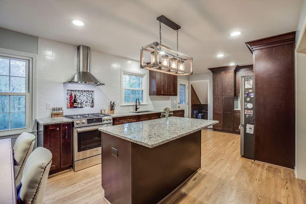 Mid-sized transitional l-shaped light wood floor and yellow floor eat-in kitchen photo in Birmingham with a double-bowl sink, shaker cabinets, dark wood cabinets, granite countertops, white backsplash, subway tile backsplash, stainless steel appliances, an island and gray countertops