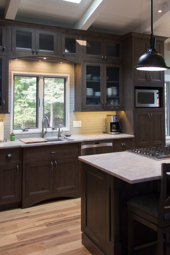 Eat-in kitchen - mid-sized transitional l-shaped light wood floor eat-in kitchen idea with an undermount sink, recessed-panel cabinets, dark wood cabinets, onyx countertops, gray backsplash, glass tile backsplash, stainless steel appliances and an island