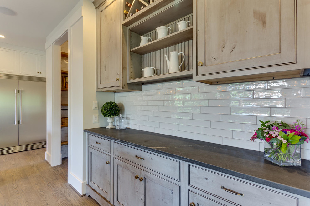 This is an example of a mid-sized transitional single-wall wet bar in DC Metro with medium hardwood floors, no sink, beaded inset cabinets, distressed cabinets, quartz benchtops, white splashback and porcelain splashback.