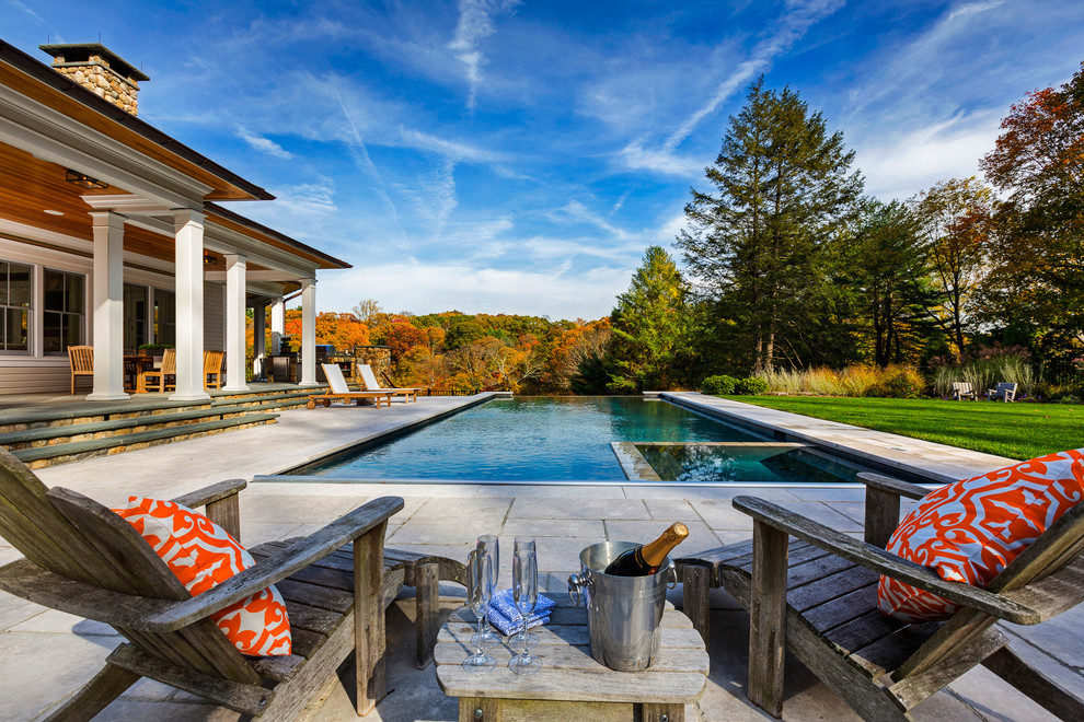 This is an example of a large traditional backyard rectangular infinity pool in New York with a hot tub and concrete slab.