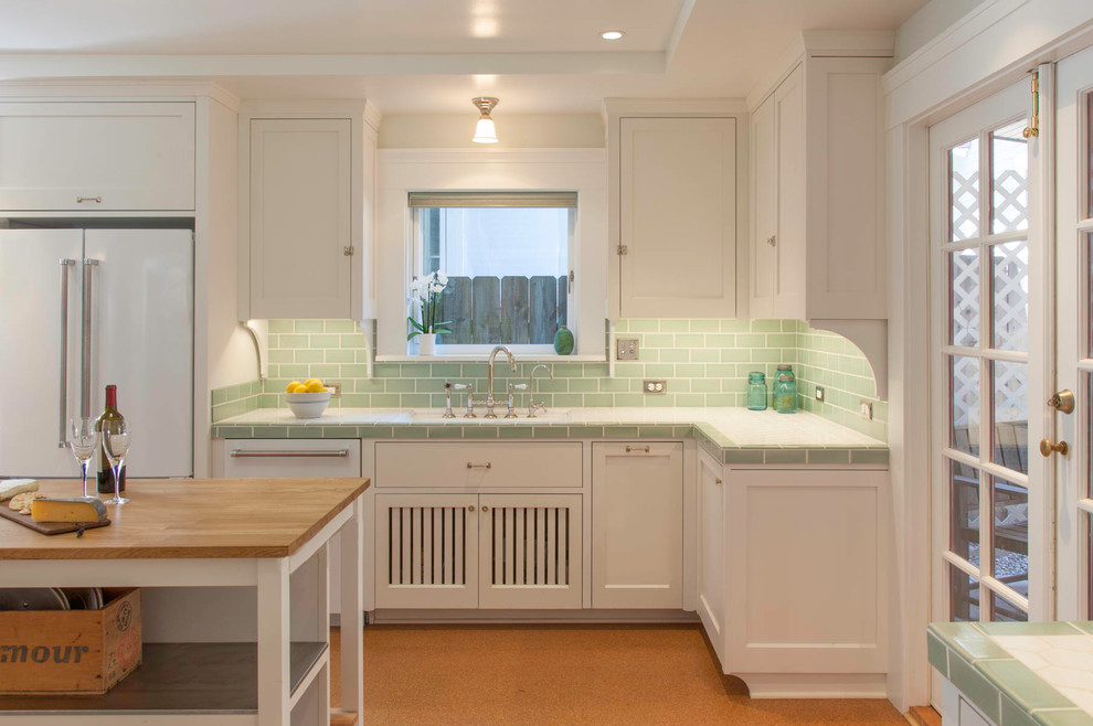 Traditional separate kitchen in San Diego with an undermount sink, shaker cabinets, white cabinets, tile benchtops, green splashback, ceramic splashback, white appliances, cork floors, with island and brown floor.