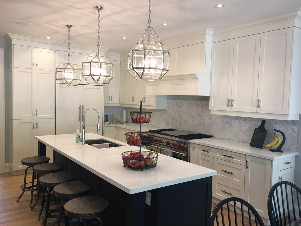 Eat-in kitchen - mid-sized transitional l-shaped medium tone wood floor eat-in kitchen idea in Toronto with a double-bowl sink, shaker cabinets, white cabinets, solid surface countertops, gray backsplash, stone tile backsplash, paneled appliances and an island