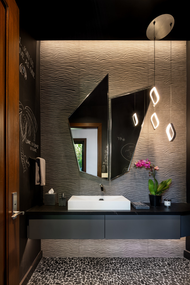 Inspiration for a contemporary powder room in Hawaii with flat-panel cabinets, grey cabinets, gray tile, pebble tile floors, a vessel sink, black floor and black benchtops.