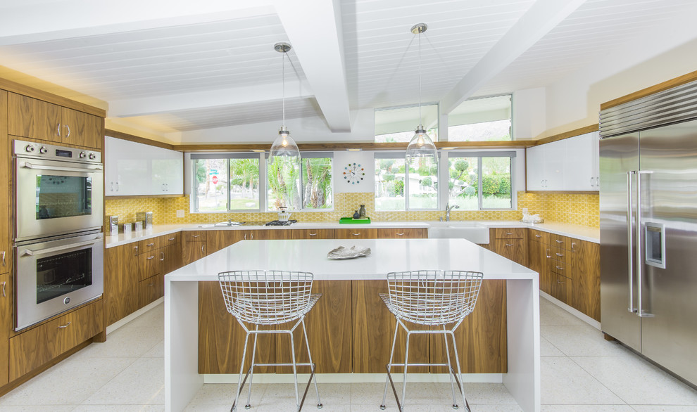 Photo of a midcentury u-shaped kitchen in Los Angeles with a farmhouse sink, flat-panel cabinets, medium wood cabinets, yellow splashback, stainless steel appliances and with island.