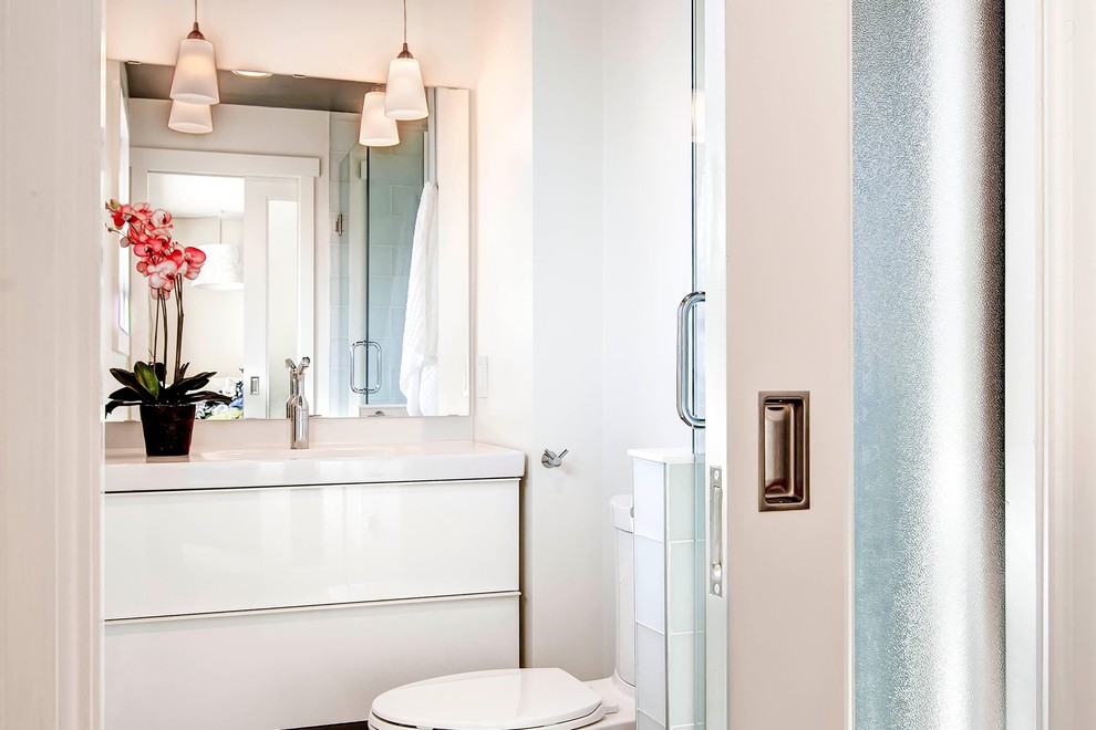 Design ideas for a mid-sized modern bathroom in Denver with flat-panel cabinets, light wood cabinets, a drop-in tub, a shower/bathtub combo, a two-piece toilet, white tile, subway tile, white walls, ceramic floors, an integrated sink and solid surface benchtops.