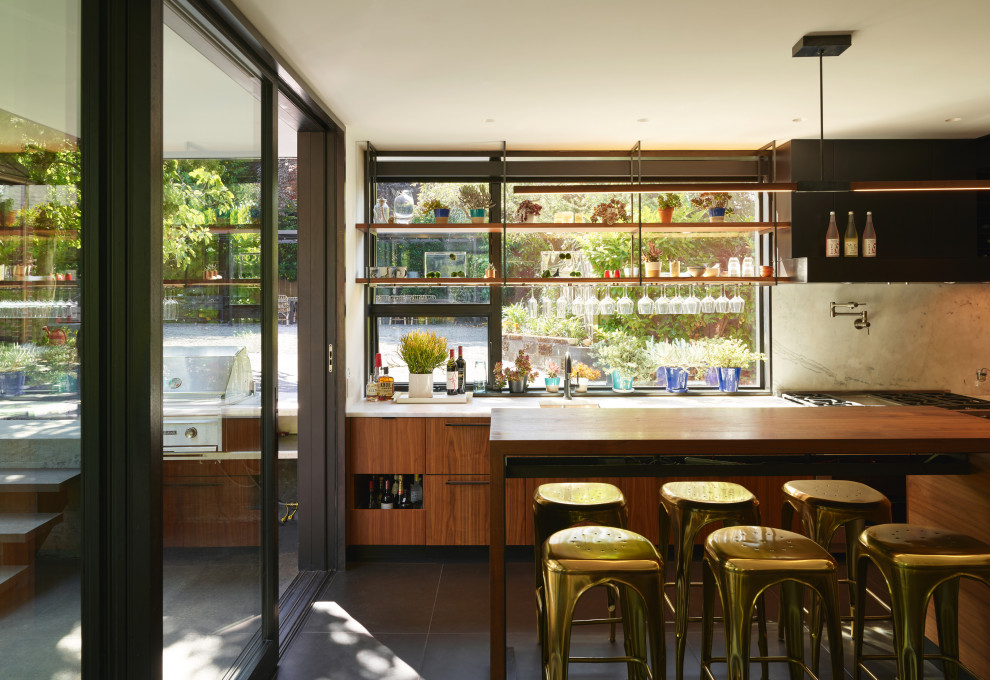 Inspiration for a large eclectic galley home bar in Seattle with an undermount sink, flat-panel cabinets, medium wood cabinets, marble benchtops, white splashback, marble splashback, black floor and white benchtop.