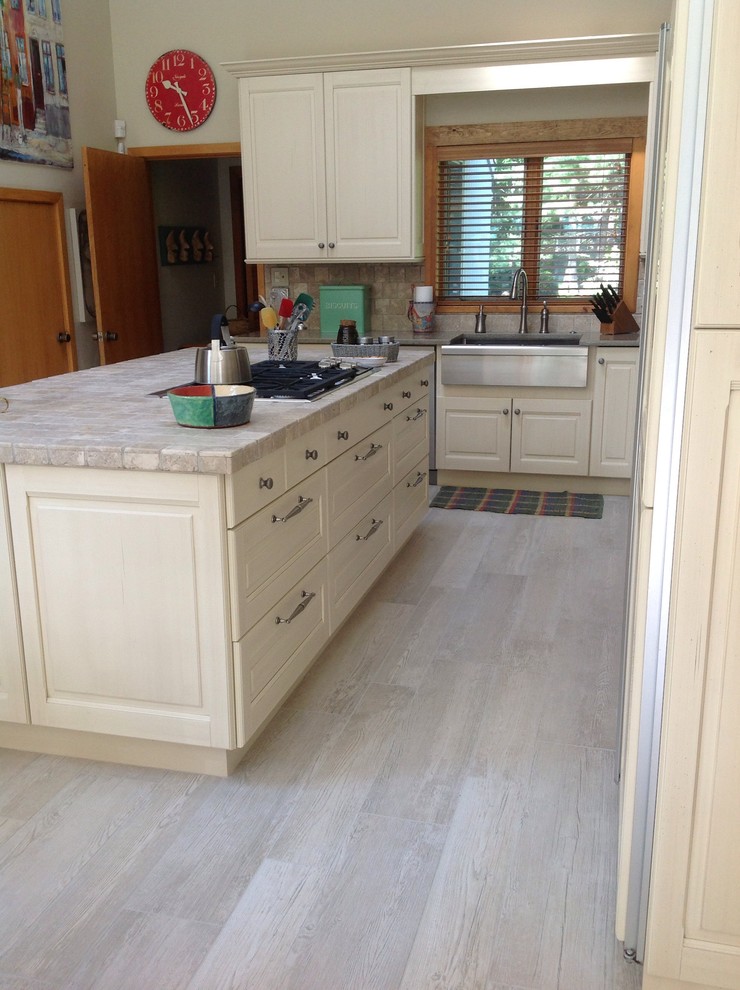 Example of a mid-sized transitional l-shaped porcelain tile and beige floor eat-in kitchen design in Boston with raised-panel cabinets, beige cabinets, an island, a farmhouse sink, tile countertops, beige backsplash, marble backsplash and paneled appliances