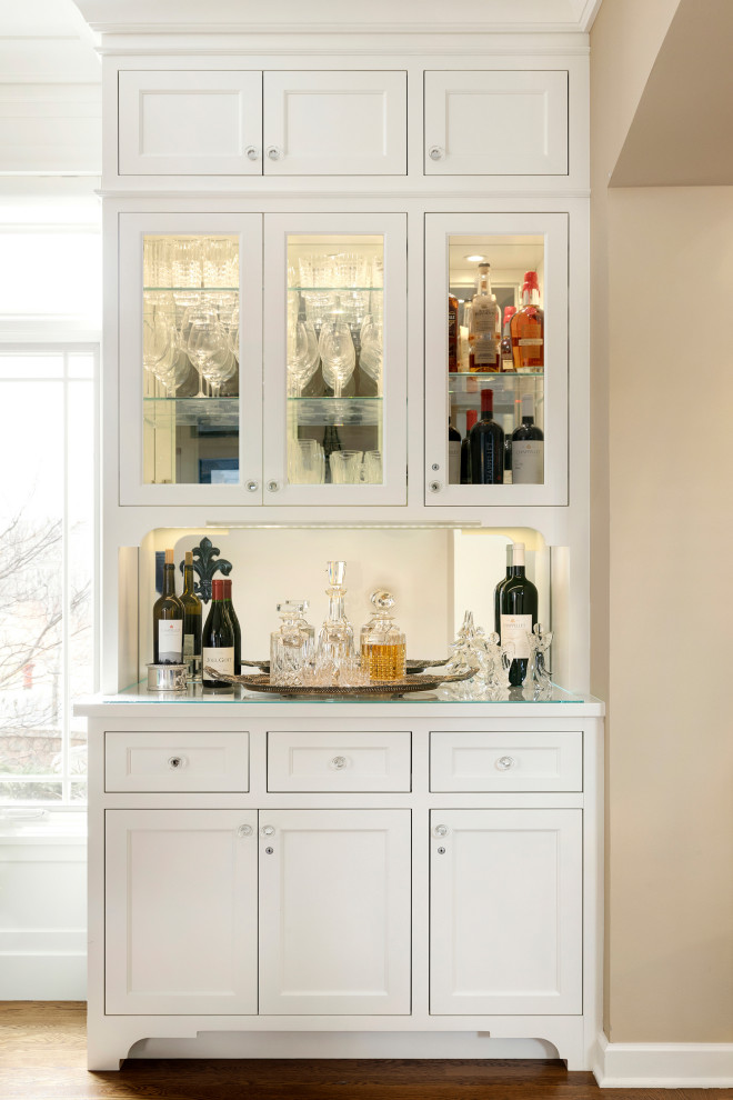 Esempio di un angolo bar senza lavandino chic con ante in stile shaker, ante bianche, top in vetro, paraspruzzi a specchio, pavimento in legno massello medio e pavimento marrone