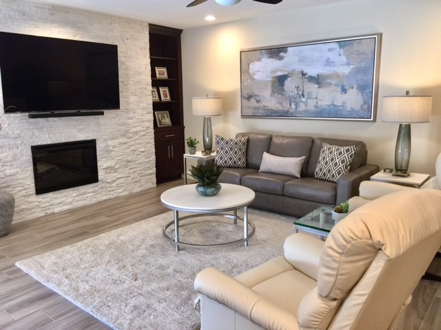 Photo of a mid-sized transitional enclosed living room in Phoenix with beige walls, vinyl floors, a standard fireplace, a stone fireplace surround, a wall-mounted tv and beige floor.