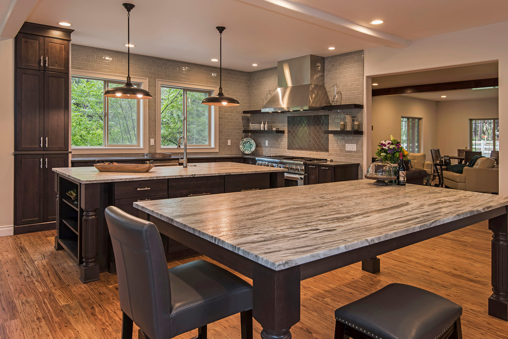 Large transitional l-shaped medium tone wood floor and brown floor open concept kitchen photo with a farmhouse sink, shaker cabinets, dark wood cabinets, granite countertops, gray backsplash, subway tile backsplash, paneled appliances and an island