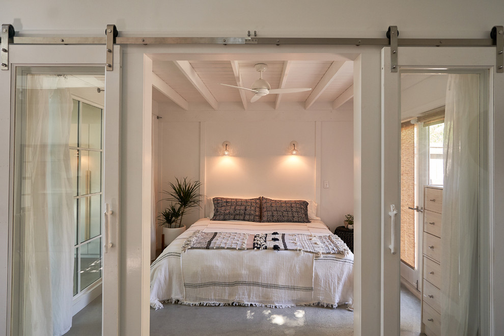 Inspiration for a mid-sized modern master bedroom in Santa Barbara with white walls, concrete floors, a plaster fireplace surround and grey floor.
